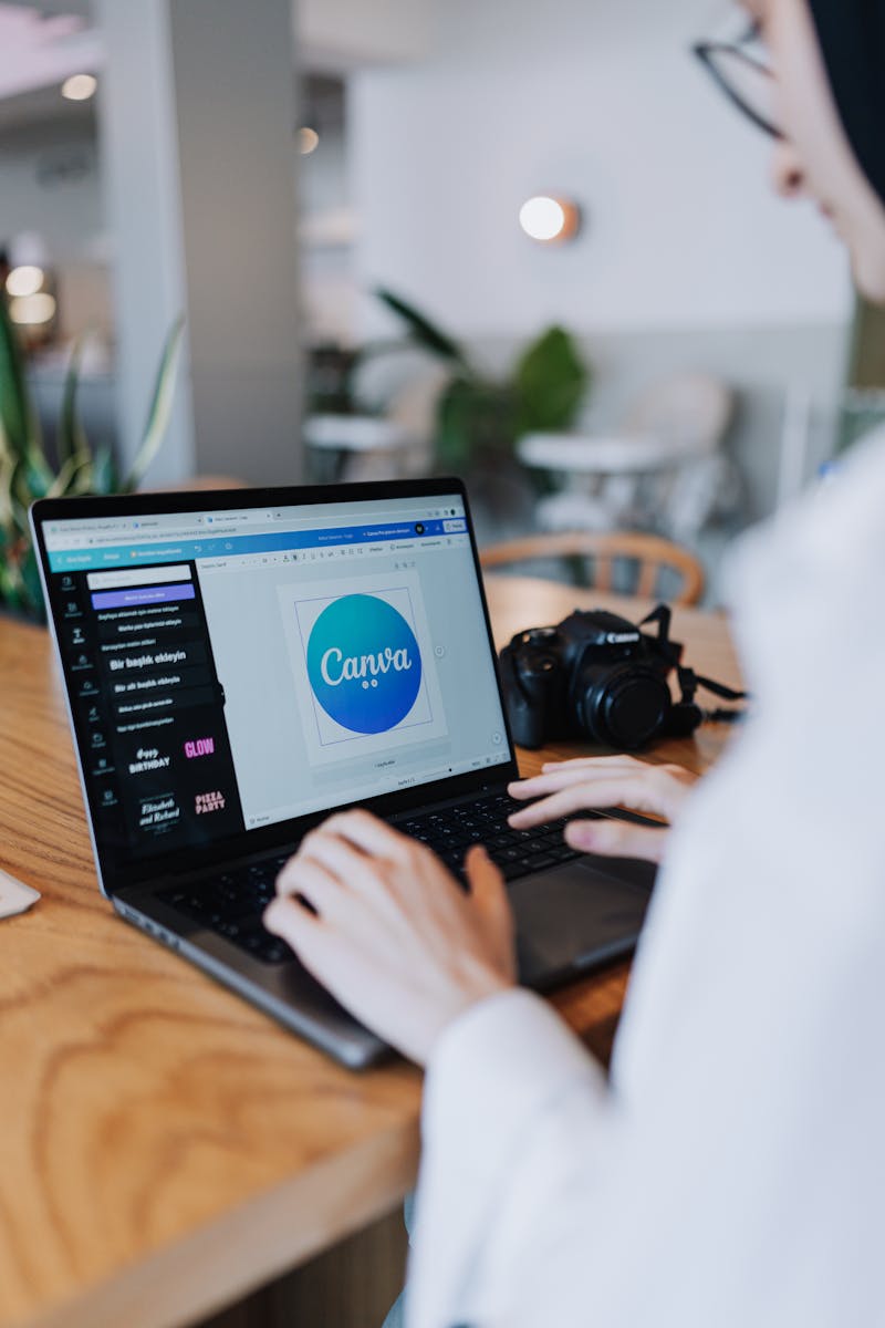 Young woman designing with Canva on laptop in a stylish indoor setting, accompanied by a digital camera.